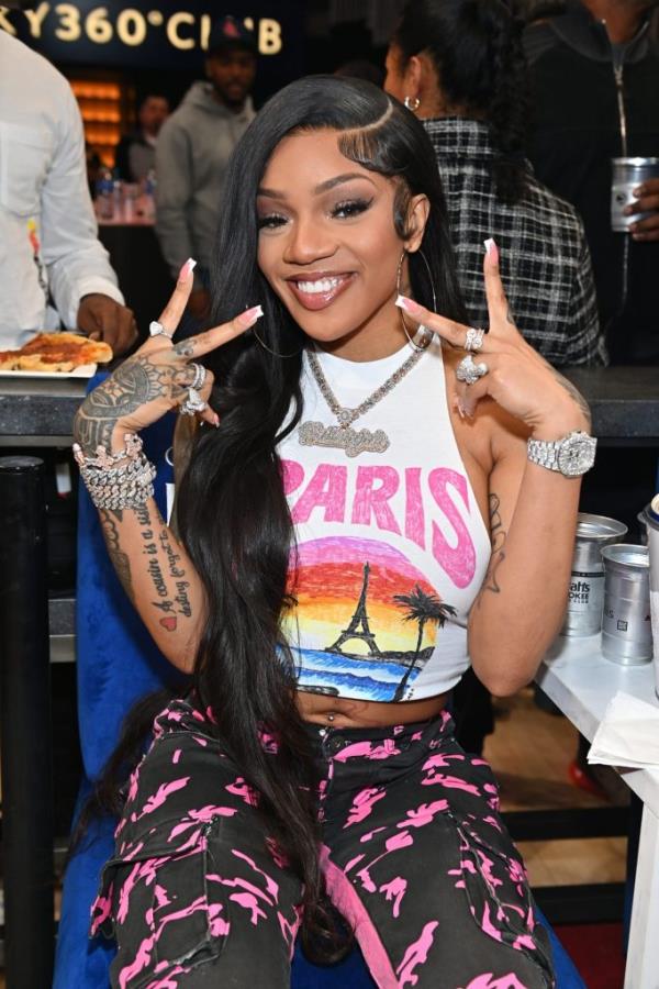 Rapper GloRilla, a Grammy-nominated artist in 2023, attending a basketball game between Golden State Warriors and Atlanta Hawks, making a hand gesture while seated at a table.