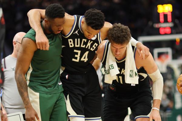 Giannis Antetokounmpo #34 of the Milwaukee Bucks is helped off the court by Thanasis Antetokounmpo #43 and Brook Lopez #11 after suffering an injury during the second half of a game against the Boston Celtics at Fiserv Forum on April 09, 2024 in Milwaukee, Wisconsin. 